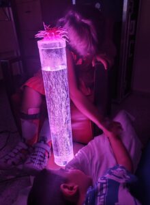 Niños interactúan junto a una columna de burbujas en una sala sensorial